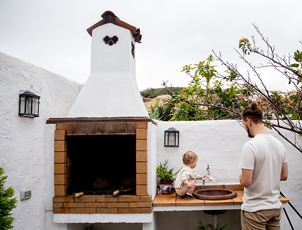 Best builder in NJ can design outdoor stoves like the white stucco one shown with tall chimney and sink on the right side where a father a child are pictured