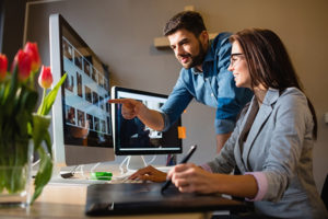 Web design Ocean County workers collaborating in front of 2 monitors examining pictures on one screen